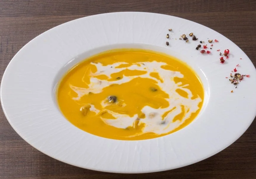 かぼちゃときのこのごちそうポタージュ。白い皿に黄色いスープとクリーム、スパイスを添えた外観。