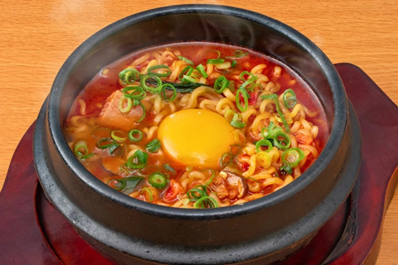 辛ラーメン。黒い器に赤いスープと麺、生卵黄、ネギが乗った辛ラーメン。
