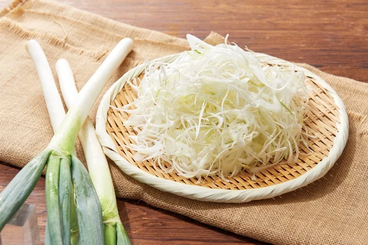 竹ざるに盛られた薄切り長ねぎと、横に置かれた生の長ねぎ