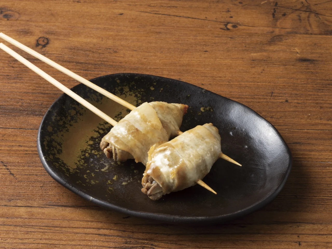 どんこ椎茸の肉巻き串。黒い皿に2本盛られた串焼き。