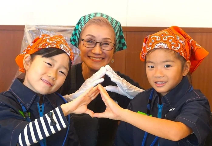 右近由美子氏と2人の子どもが手袋をしてハート形の手を組む親子おむすび教室の様子