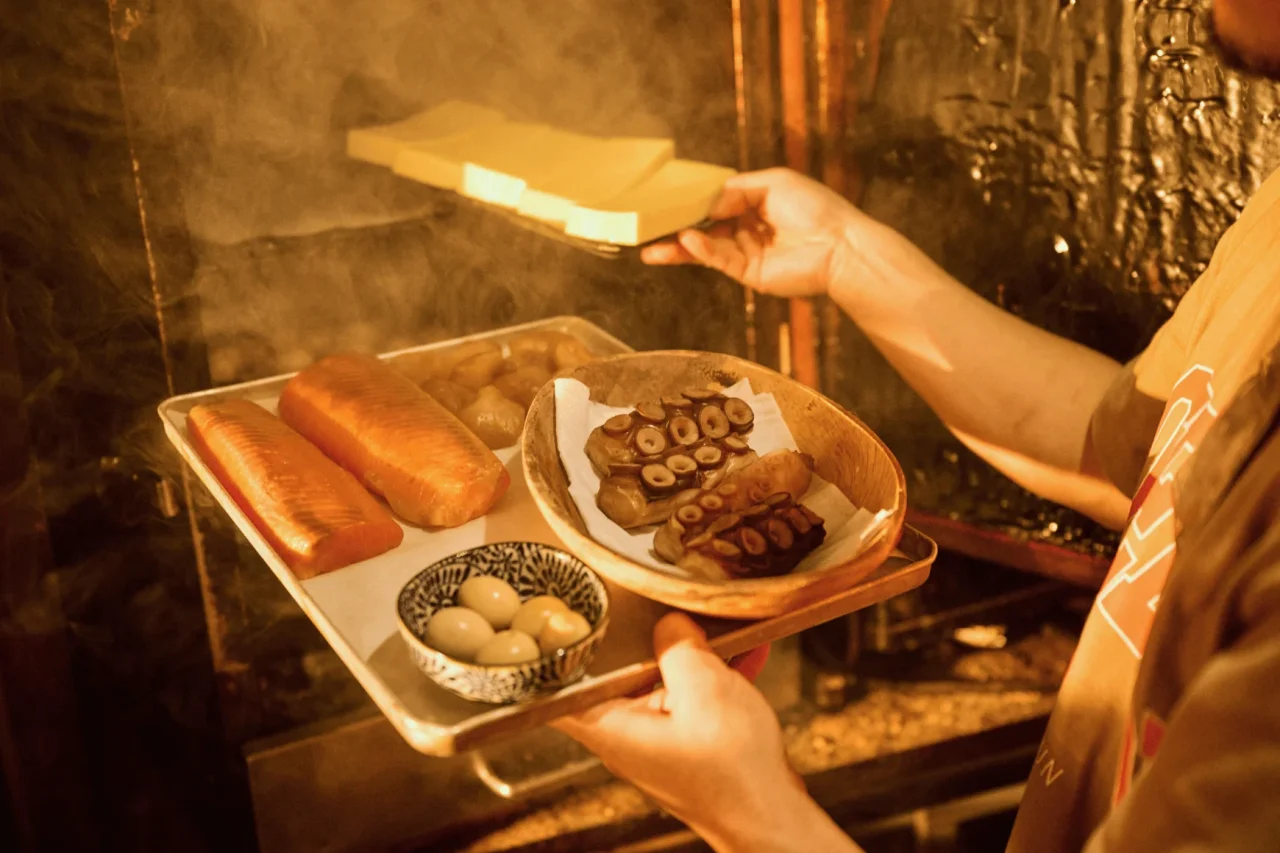 燻製料理を並べたトレイを手にするスタッフと、煙が立ち込める店内の風景