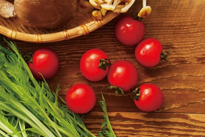 木製テーブルに並べられた赤いチェリートマトと緑の葉物野菜