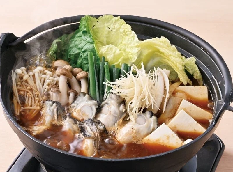 牡蠣の土手鍋。黒い鍋に牡蠣・きのこ・豆腐・白菜・ネギが盛り込まれた鍋料理
