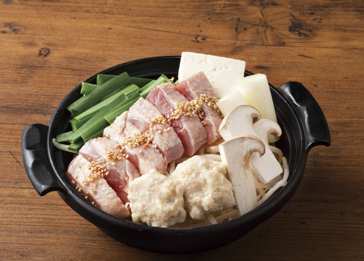 名古屋コーチンの水炊き鍋。黒い鍋に鶏肉、豆腐、ネギ、キノコが盛り付けられている