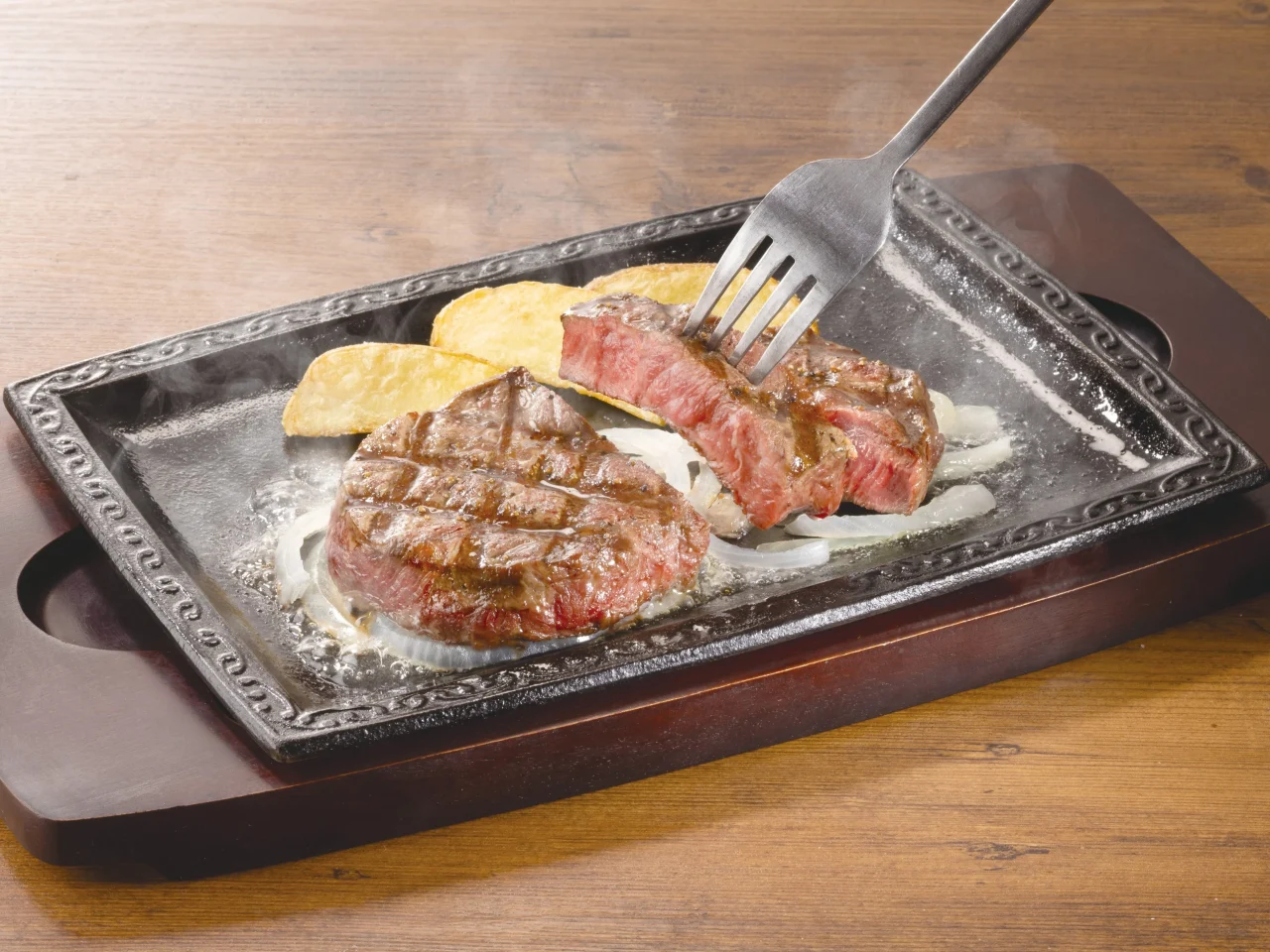 ステーキガストの熟成みすじステーキ。鉄板に盛られ、フォークで切り分けた断面とポテトが写る。