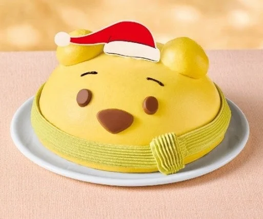 サンタ帽子をかぶったくまのプーさんの顔が描かれた黄色いクリスマスケーキ