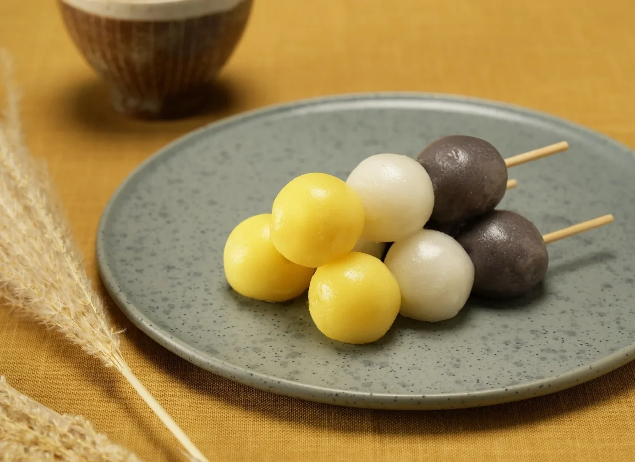芋栗月見団子。黄・白・紫の三色団子が串に刺さり、青い皿に盛られています。