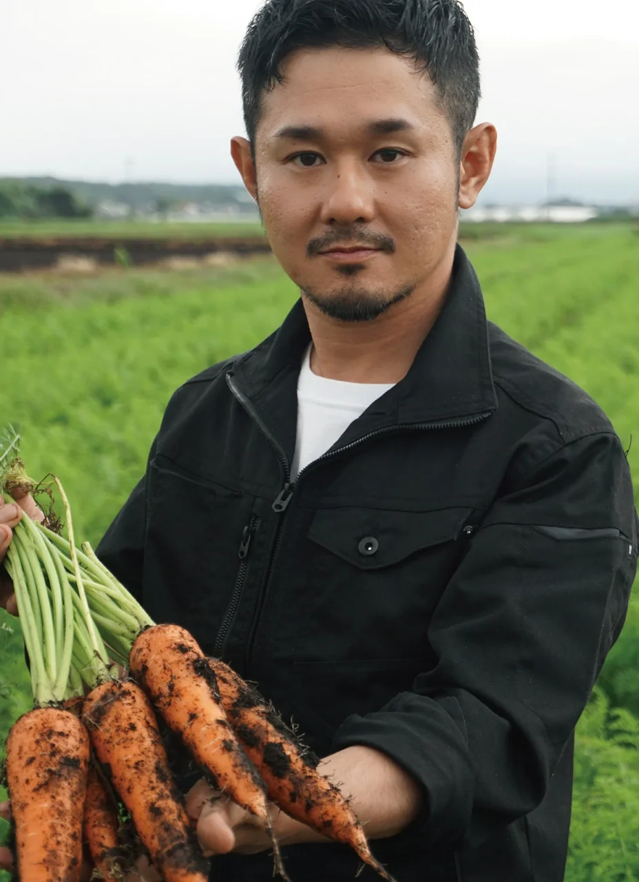 火の国ファーム本田晃久さんが畑で収穫した人参を手にしている