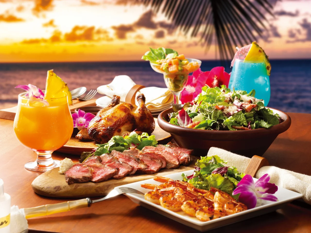 La Ohanaの店内飲食イメージ。海辺のテーブルに焼鳥、ステーキ、サラダ、エビ、カクテルが並ぶ