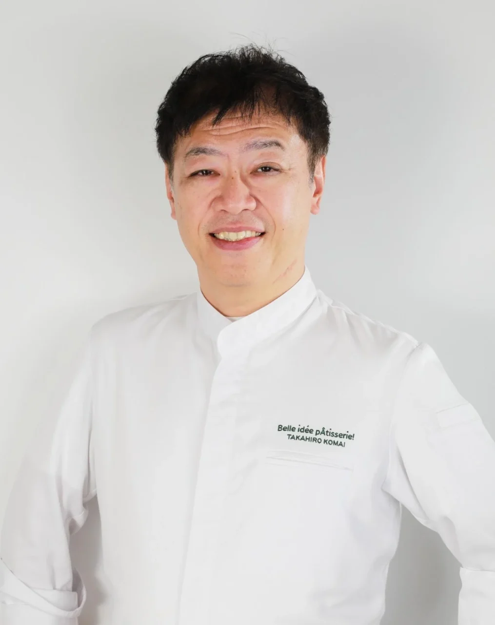 駒居崇宏シェフのポートレート。白いシェフコートを着用し、胸元に「TAKAHIRO KOMAI」の文字
