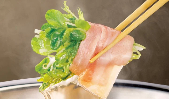 箸で豆苗を豚肉で巻いた巻きしゃぶを鍋から持ち上げる様子