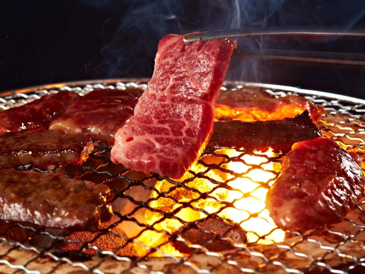 じゅうじゅうカルビの網焼き肉。ハサミで肉を持ち上げ、火加減を確認する様子。