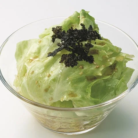 ガラスの器に盛られたレタスのサラダで、黒い海苔とごまがトッピングされている