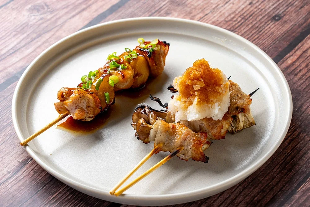 舞茸の肉巻き串～おろしポン酢～の焼き鳥串2本を白い皿に盛り付けた写真