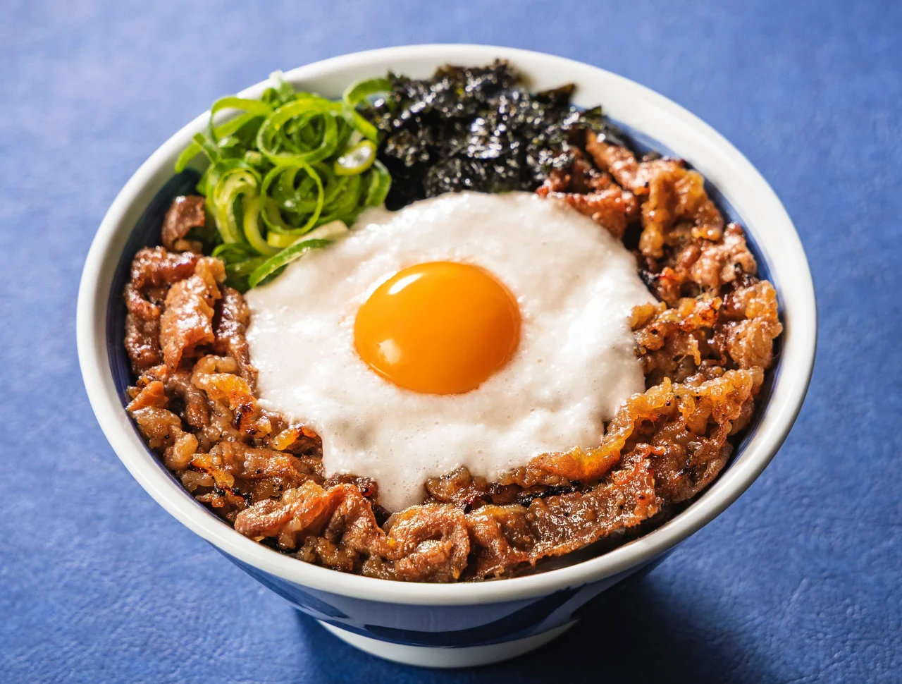 月見とろろカルビ丼(元祖盛)の丼。中央に卵黄、周囲にネギと海苔