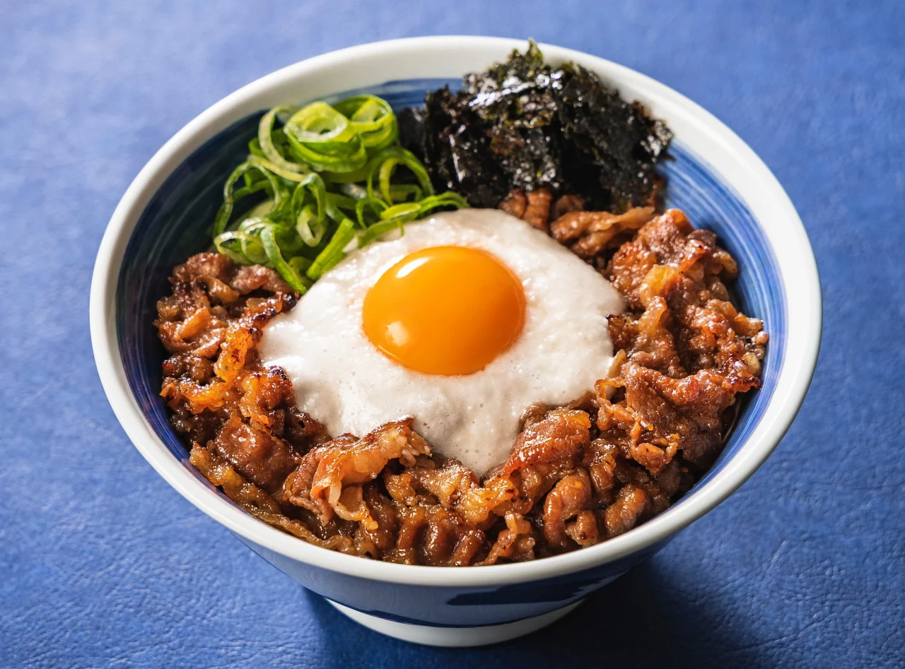 月見とろろカルビ丼(並盛)の丼。中央に卵黄、周りにネギと海苔を添えた外観。