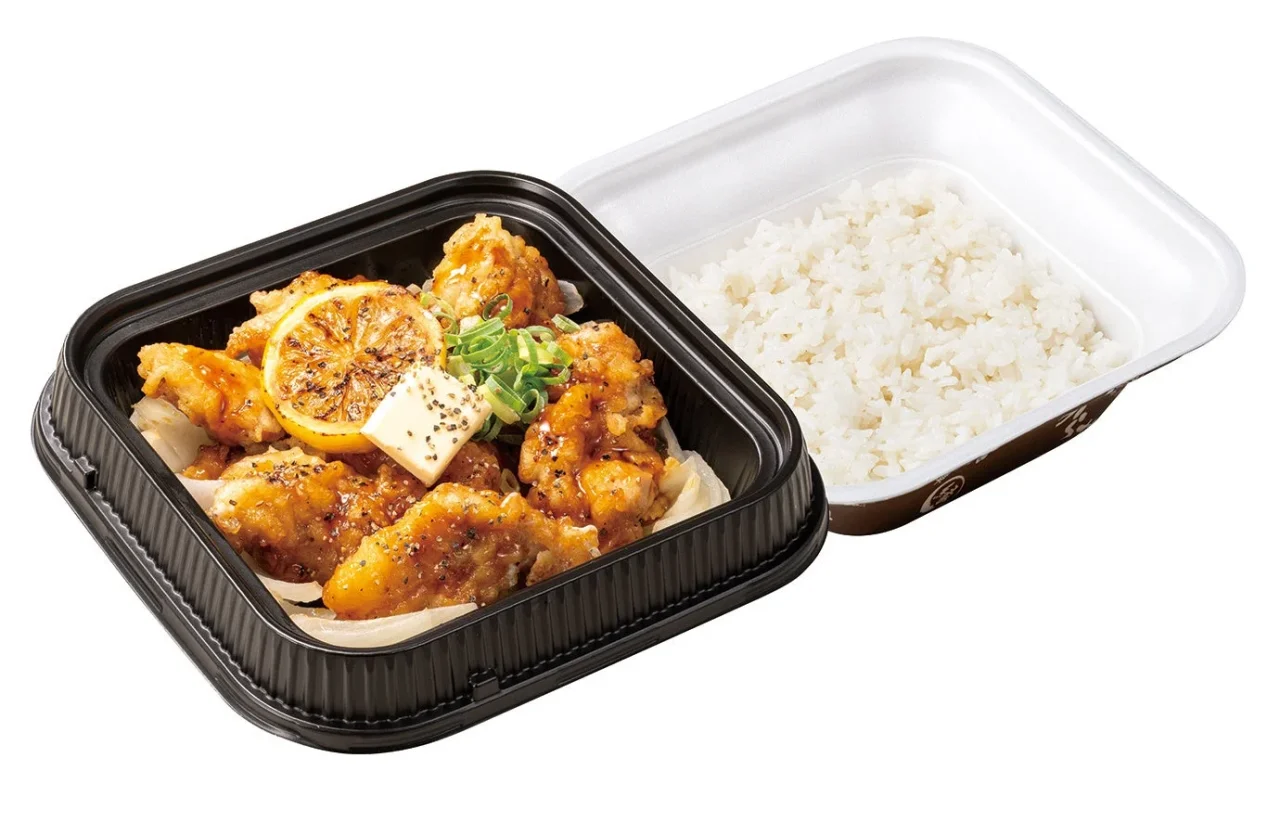 黒胡椒とり天のレモンステーキ弁当。黒い容器にソースをかけたからあげ、焼きレモン、ネギ、バター、ご飯が入ったテイクアウト弁当。