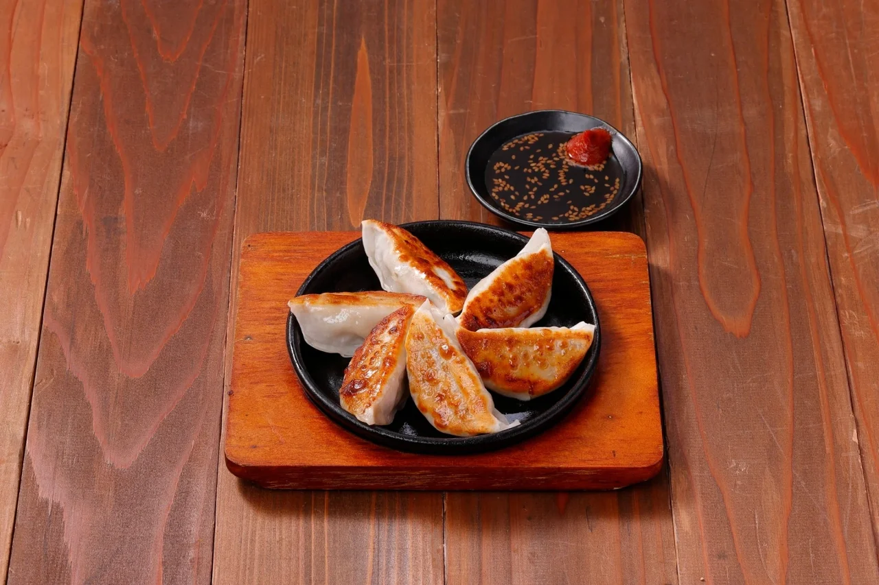 国産鶏と野菜の鉄板餃子。黒皿に並べた餃子と、ごまポン酢と辛みそが添えられた小皿。
