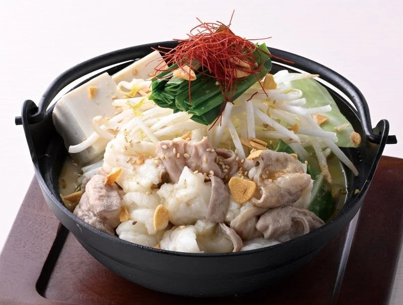 もつ鍋。黒い鉄鍋にもつ・豆腐・もやし・白菜・ニラを盛り付け、味噌仕立てのスープで煮込む