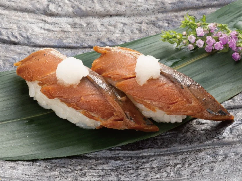 《福井若狭の郷土料理》鯖のへしこ炙り。葉の上に2貫の握り寿司が並ぶ。