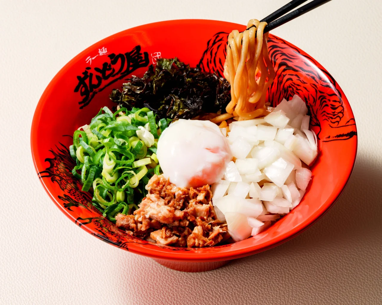 ラー麺ずんどう屋の『濃厚豚骨まぜそば』。赤い丼に極太麺、温玉、バラチャーシュー、刻みねぎ、玉ねぎ、のりが盛り付けられている。