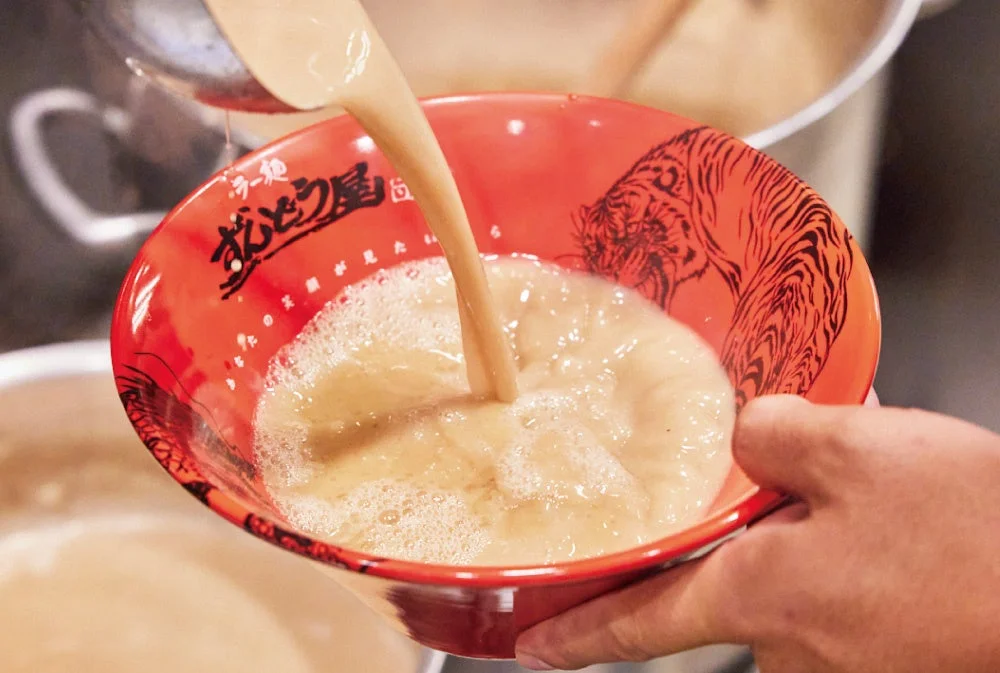 ラー麺ずんどう屋の赤い丼に濃厚豚骨スープを注ぐ様子