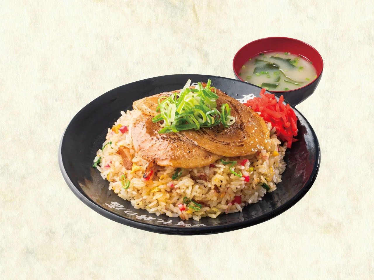 黒い皿にチャーシューをのせた焼豚チャーハンと味噌汁