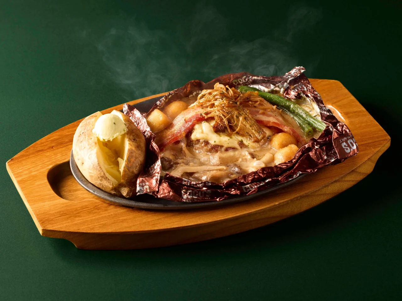 ココスのポルチーニ香るたっぷりきのこの包み焼きハンバーグ。アルミホイルで包み焼きにしたハンバーグにきのこやベーコンを添え、ベイクドポテトと共に出汁が立つ様子。