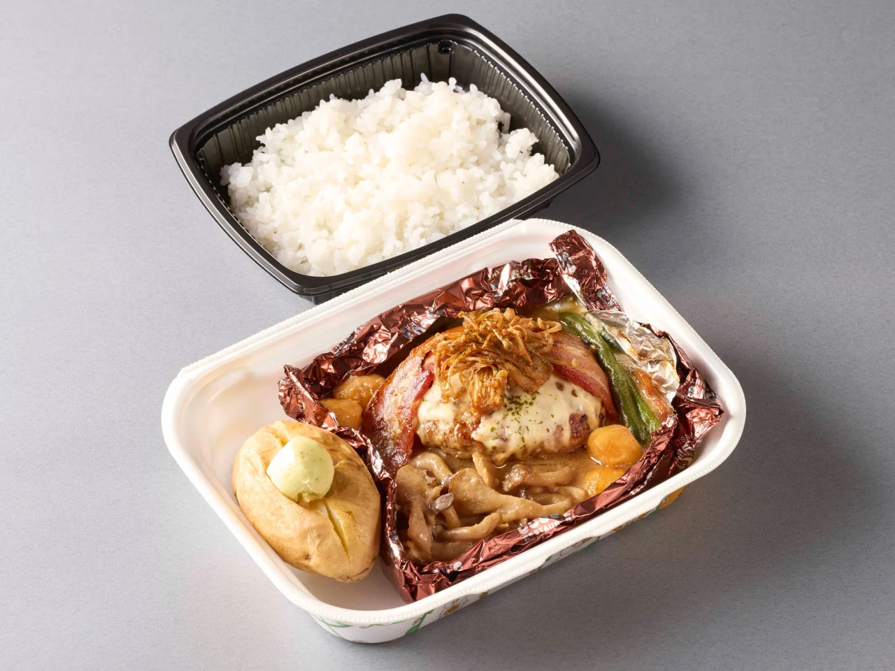 ポルチーニ香るたっぷりきのこの包み焼きハンバーグ弁当。アルミホイルで包まれたハンバーグときのこ、ベイクドポテト、ご飯が写る。
