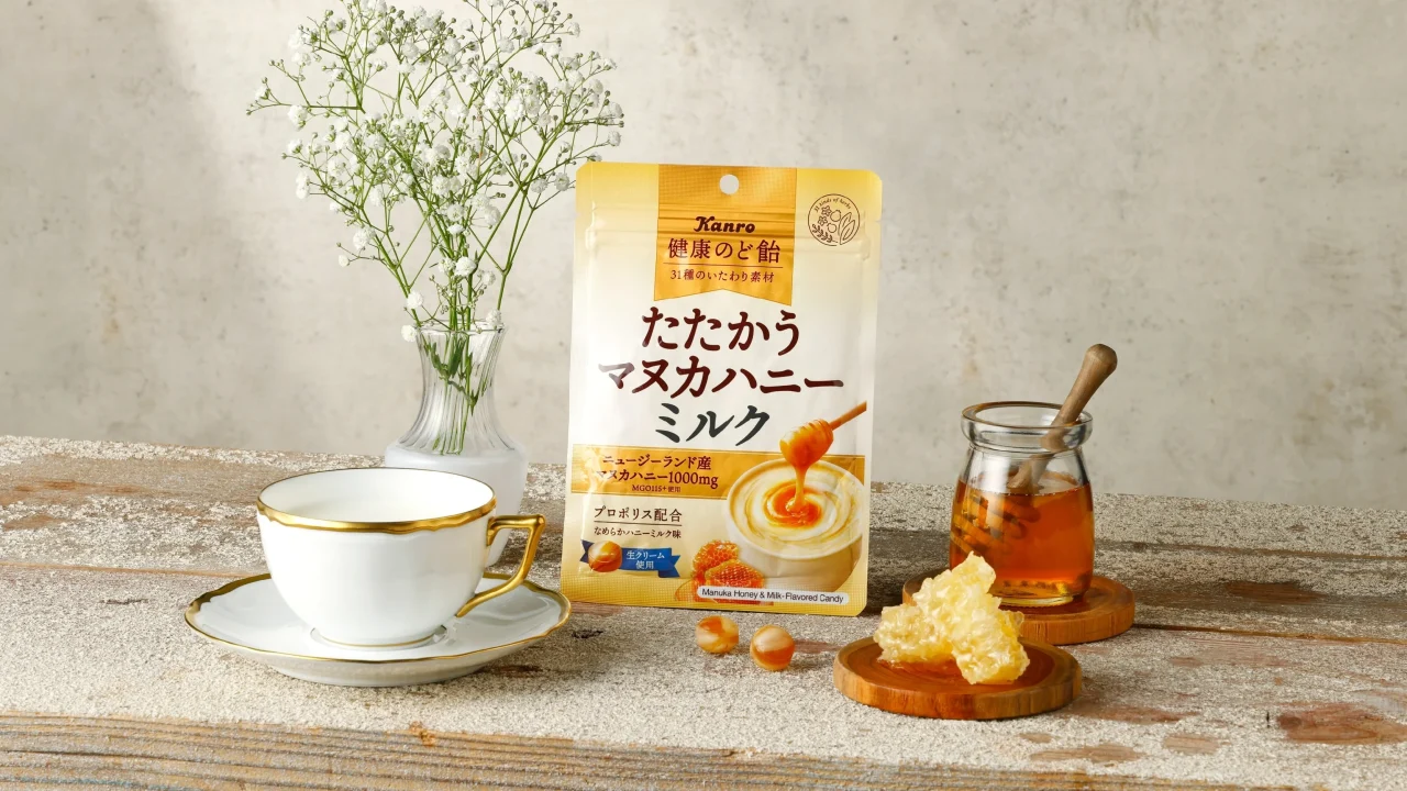健康のど飴たたかうマヌカハニーミルクのパッケージと、はちみつやティーカップが並ぶ静物写真