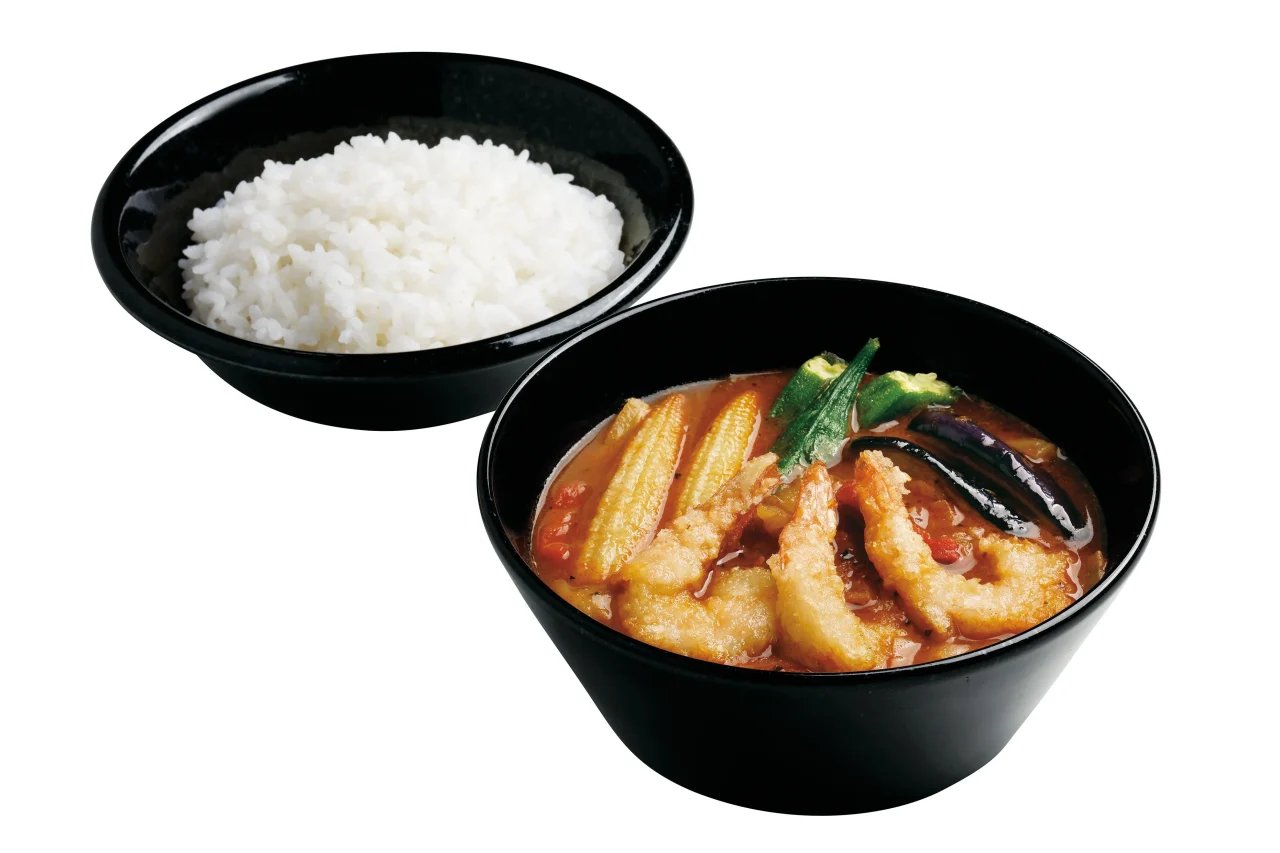 トムヤムクンスープカレーと白米。海老や野菜が乗ったスープカレーと、黒い器に入った白米が並ぶ。