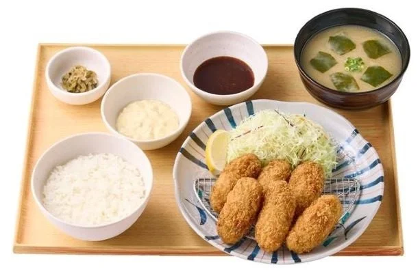 ~濃厚な海の恵み~かきフライ定食(6個)の提供写真。木製トレイに6個のかきフライ、ご飯、味噌汁、ソース、タルタルソース、レモン、キャベツが並ぶ。