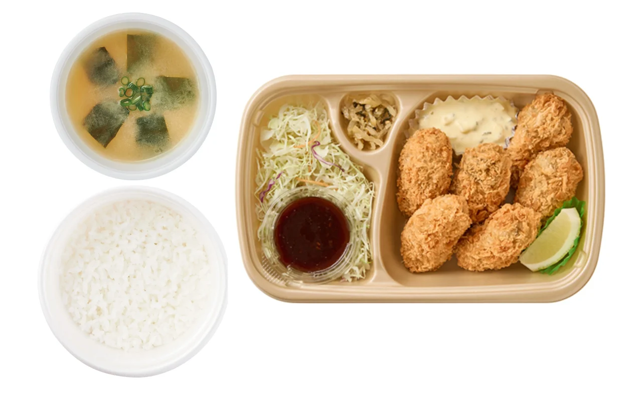 テイクアウト用のかきフライ6個定食。弁当箱に衣をまとったかきフライ6個、ソース、タルタル、サラダ、レモン、ご飯、味噌汁が写る。