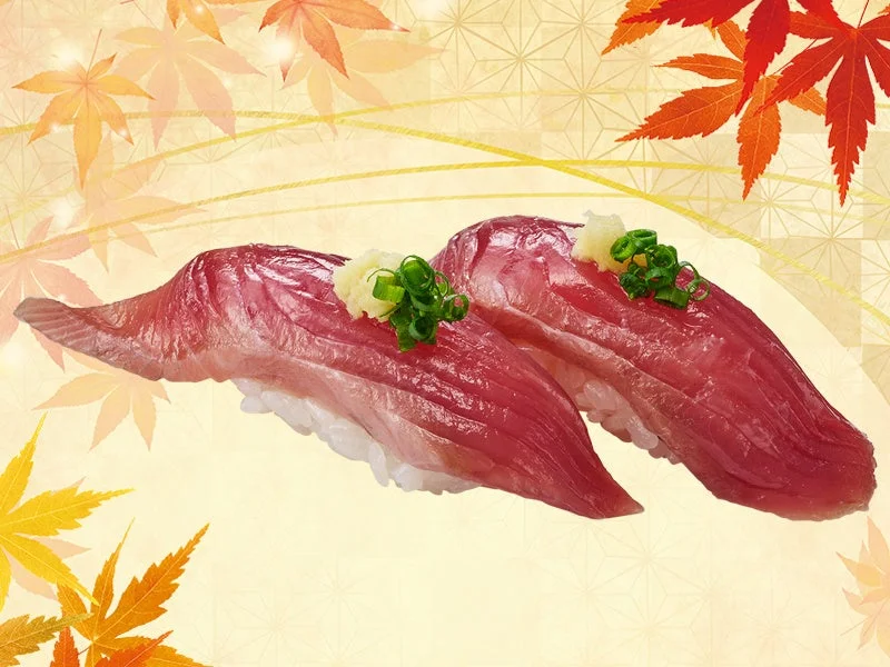 とろ鰹の握り寿司2貫。赤身の魚に生姜とネギを添え、秋の紅葉を背景に配置。