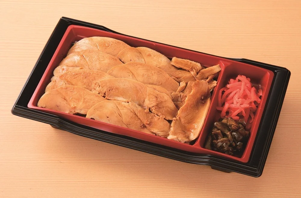 黒い容器に入った群馬名物とり重。薄くスライスした鶏むね肉がご飯の上にのっており、小鉢には赤い漬物と煮物が入っている。