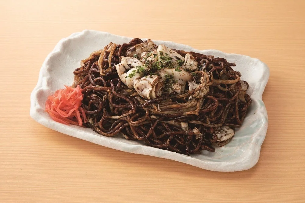 太田焼きそば。いか墨ソースで黒く絡めた麺とイカ、紅生姜を盛り付けた様子。