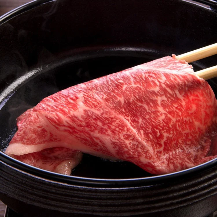 すき焼き鍋で箸で持ち上げられた霜降りの黒毛和牛モモ肉
