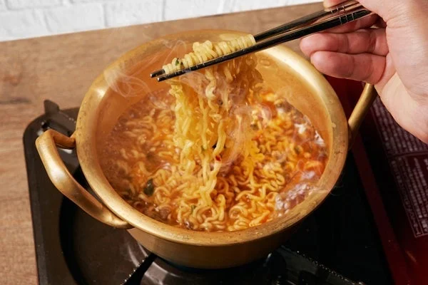 卓上コンロで煮込まれる赤いスープの鍋料理。箸で麺をすくう様子。