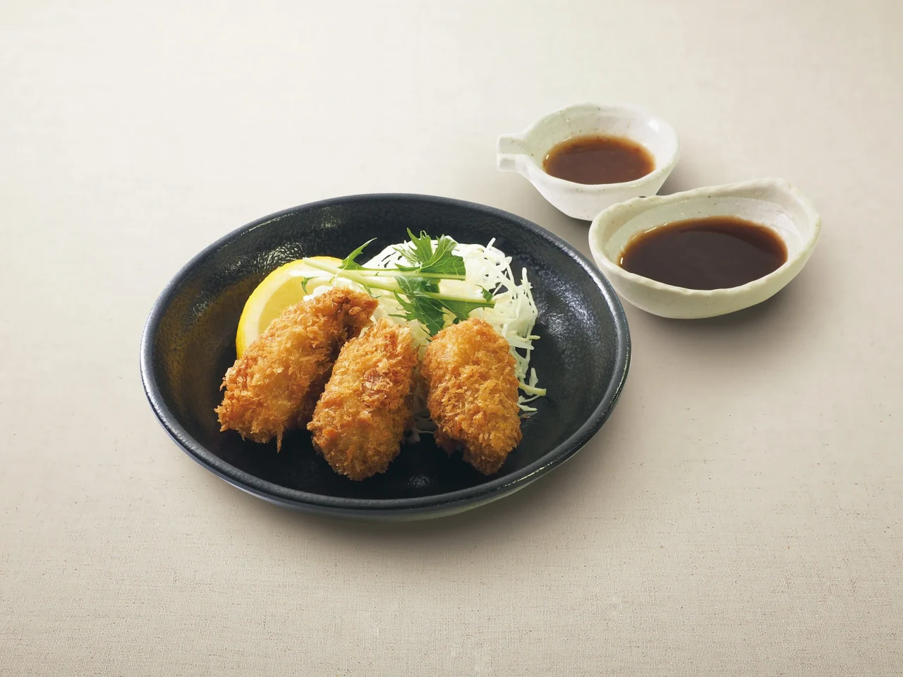黒い皿に盛られた3個の牡蠣フライとソースの小皿