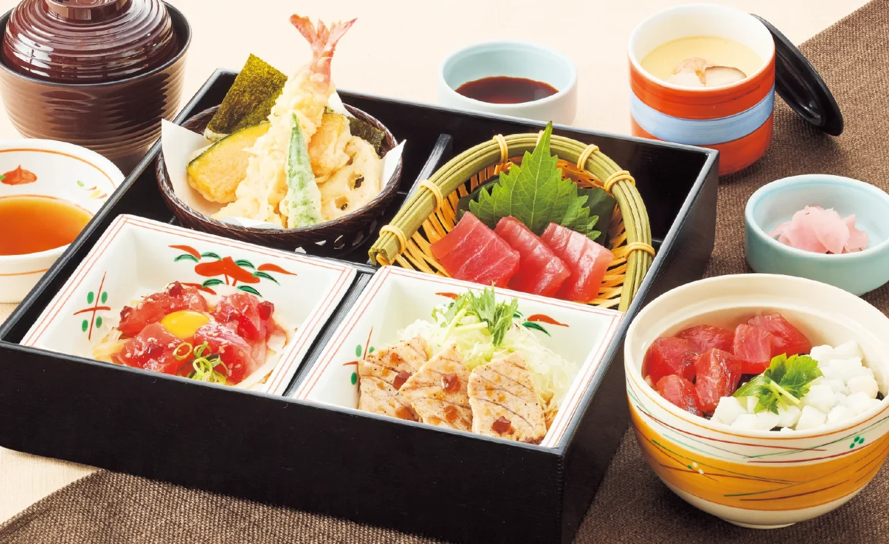 鮪づくし御膳。黒い重箱に刺身・ユッケ風・ステーキ・丼、天ぷら、茶碗蒸しを盛り付けた様子。