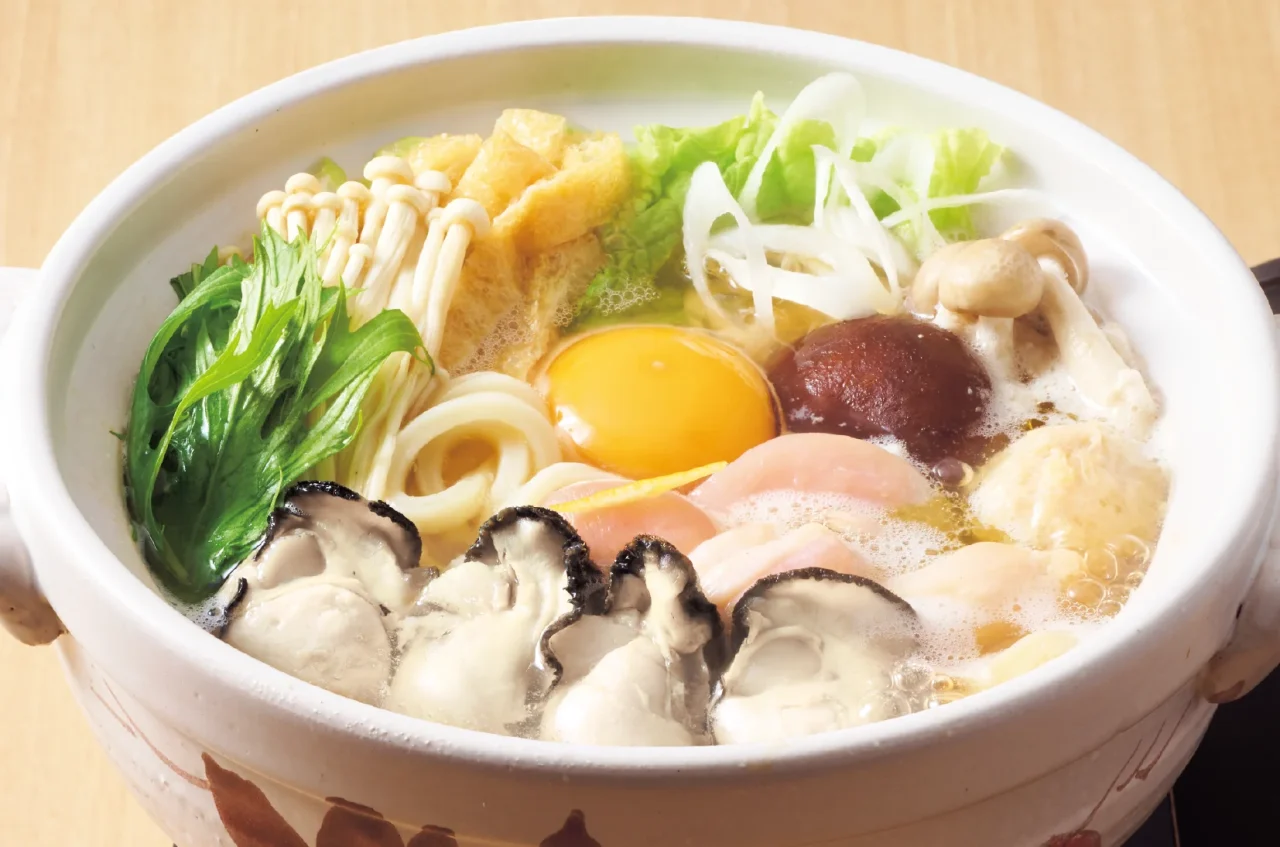 牡蠣入り鍋焼きうどん。牡蠣、生卵、きのこ、野菜、うどんが入った器
