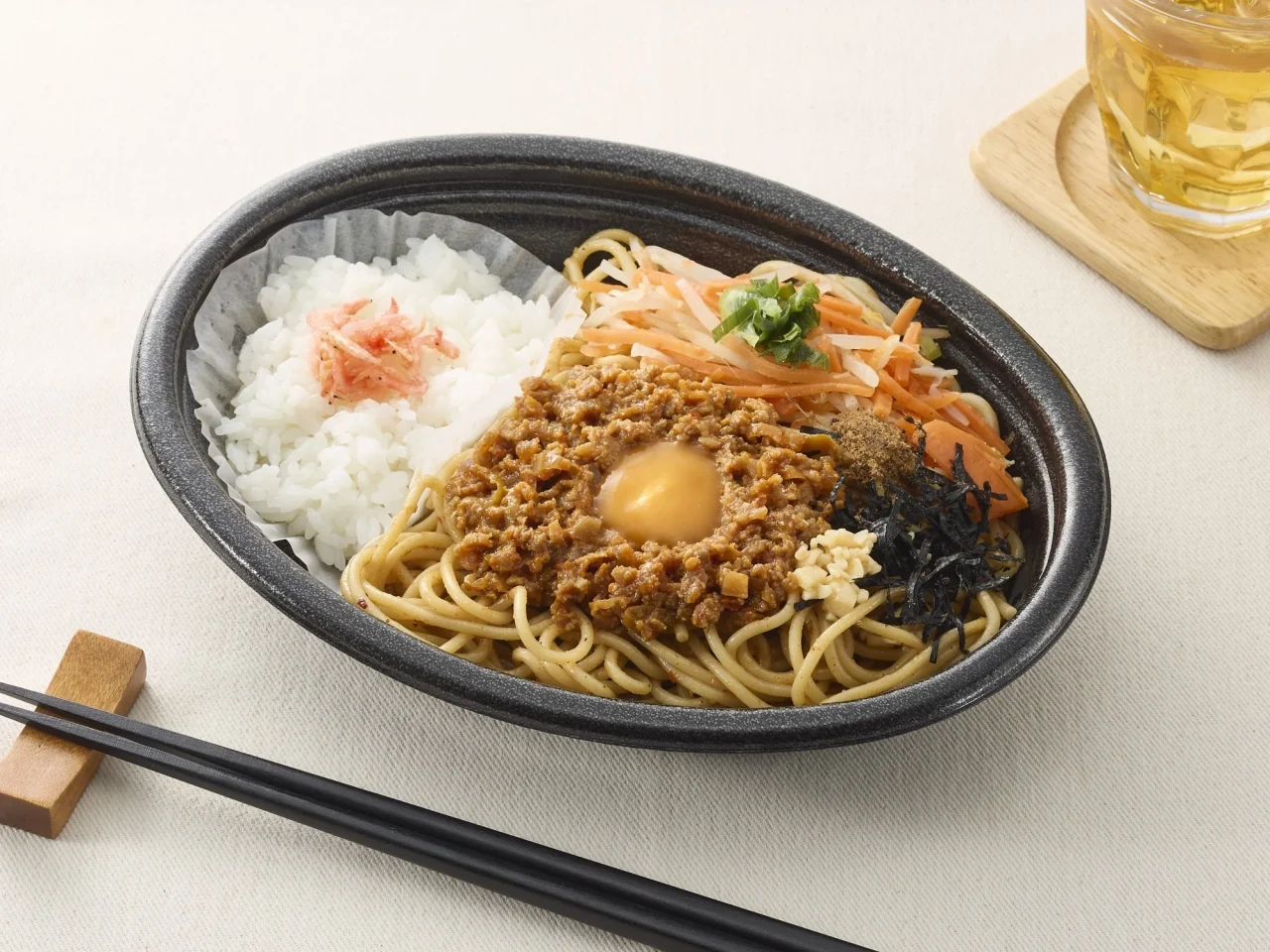 汁なし台湾風まぜ麺弁当(追い飯付き)の通常サイズ。黒い器に麺、挽肉、生卵、白米、具材が盛り付けられている。