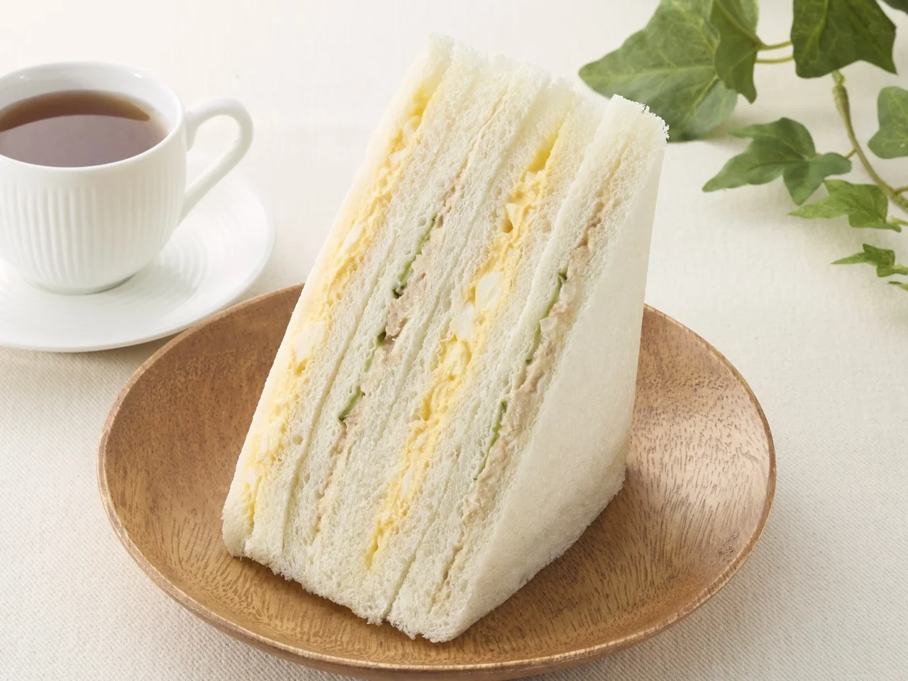 ツナたまごサンドの増量イメージ画像。木皿に盛られたサンドイッチとコーヒーが写っている。