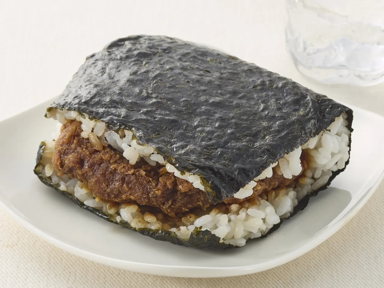 サンドおむすび味噌カツ(大麦入り)の通常サイズで、海苔に包まれたおむすびに味噌カツが挟まれている