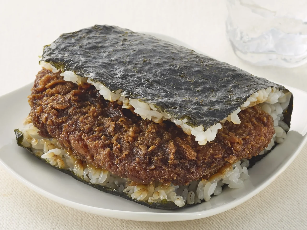 サンドおむすび味噌カツ(大麦入り)の増量イメージ画像。海苔で包まれたおむすびに、厚みのある味噌カツが挟まれています。