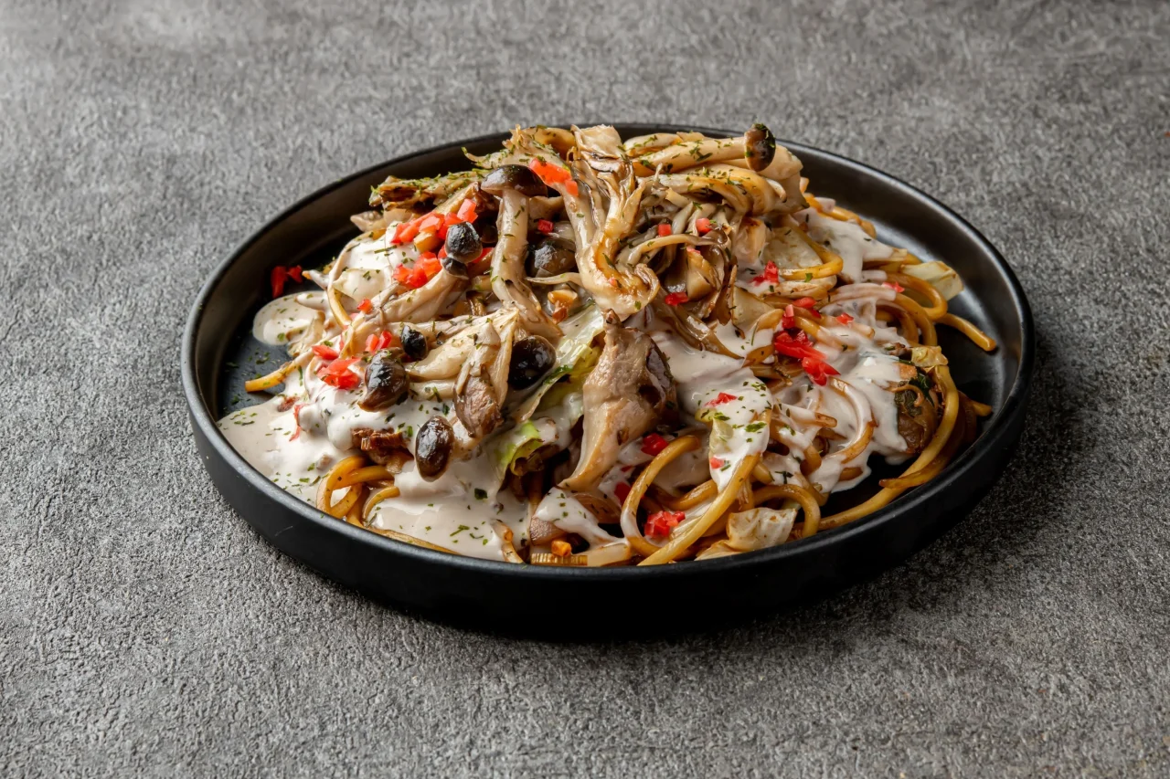 黒い皿にキノコとクリームソースをかけた焼そば