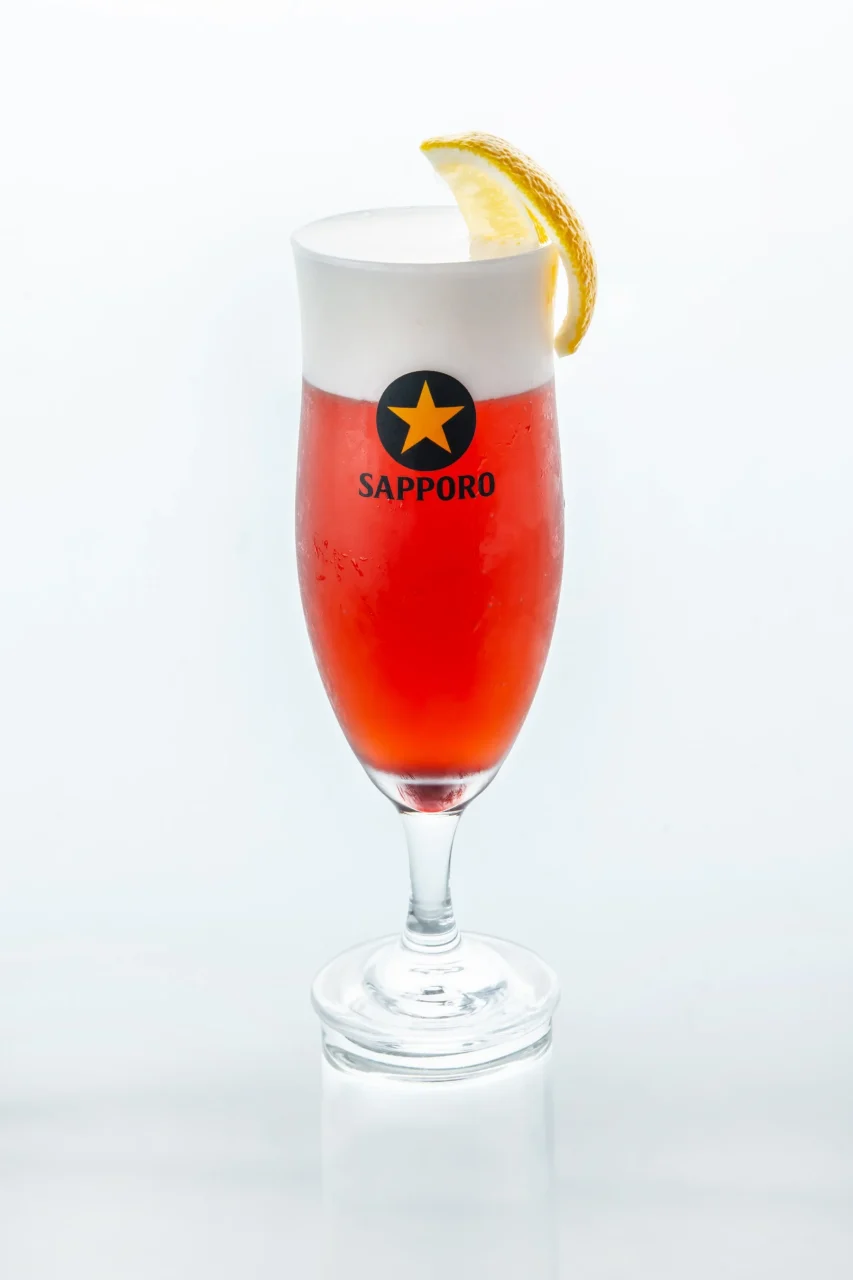 カシスビール。ルビー色の液体に白い泡とレモン輪が添えられたグラス。