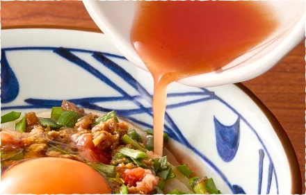 肉辛まぜうどんの具材にトマト酢を注ぐ様子