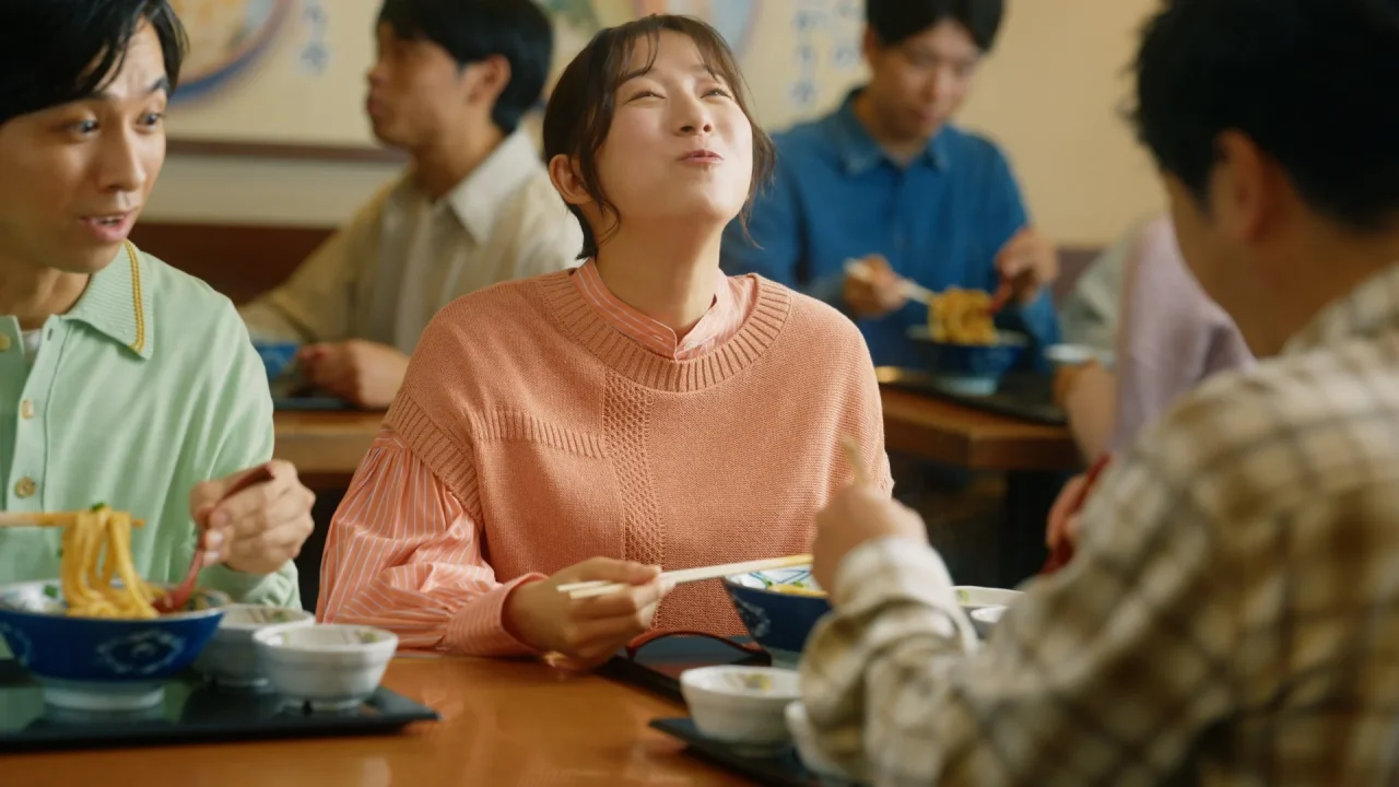 丸亀製麺のTVCMカット。店内でうどんを食べる女性と周囲の客のシーン。